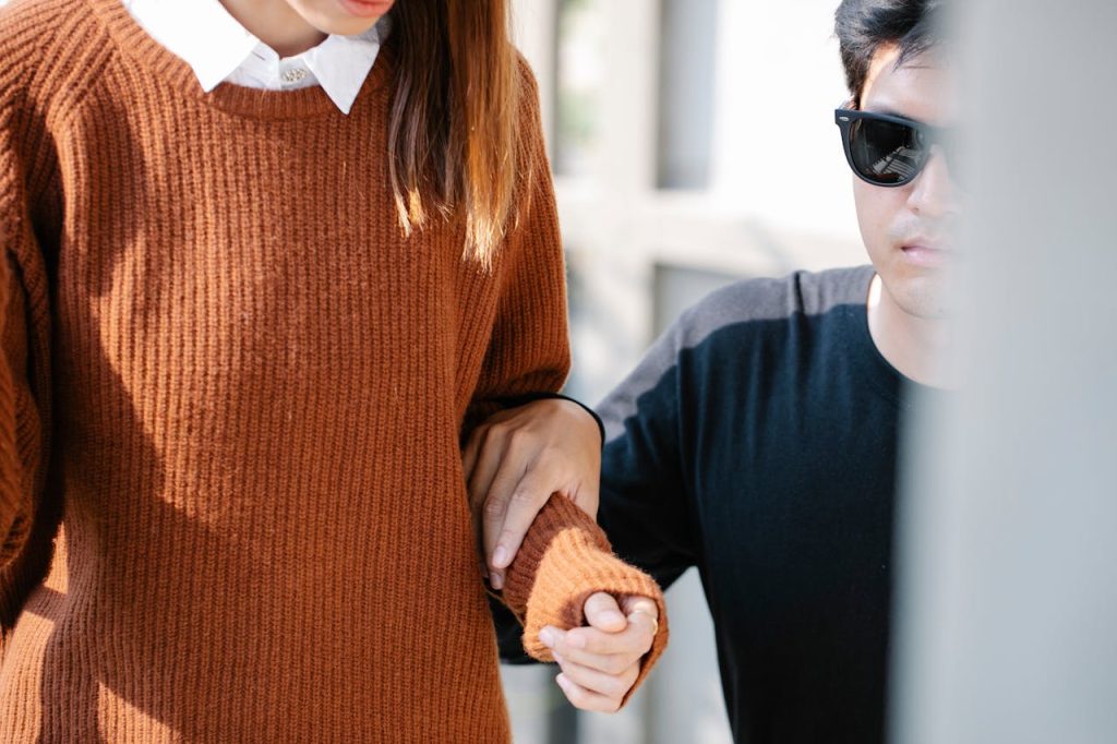A man wearing sunglasses guides a visually impaired woman outdoors, highlighting care and assistance.